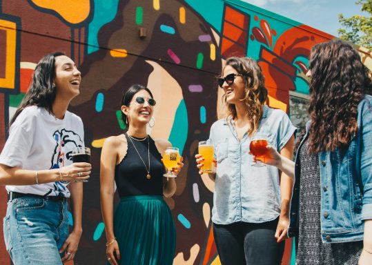 vier Frauen stehen und lächeln und prosten sich zu