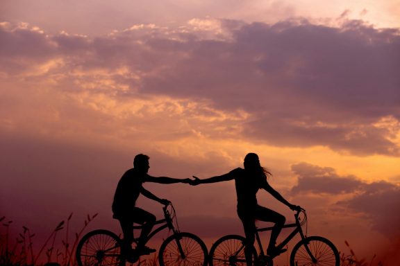 zwei Menschen reichen sich auf dem Fahrrad bei Sonnenuntergang die Hand